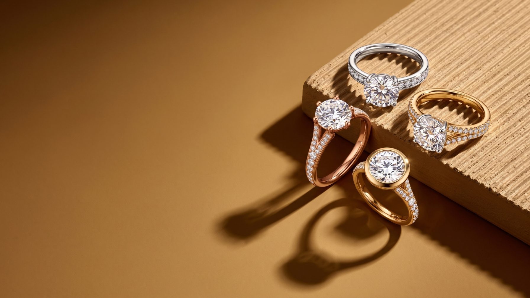 Four diamond engagement rings in white, yellow and rose gold on a sculpted stone block